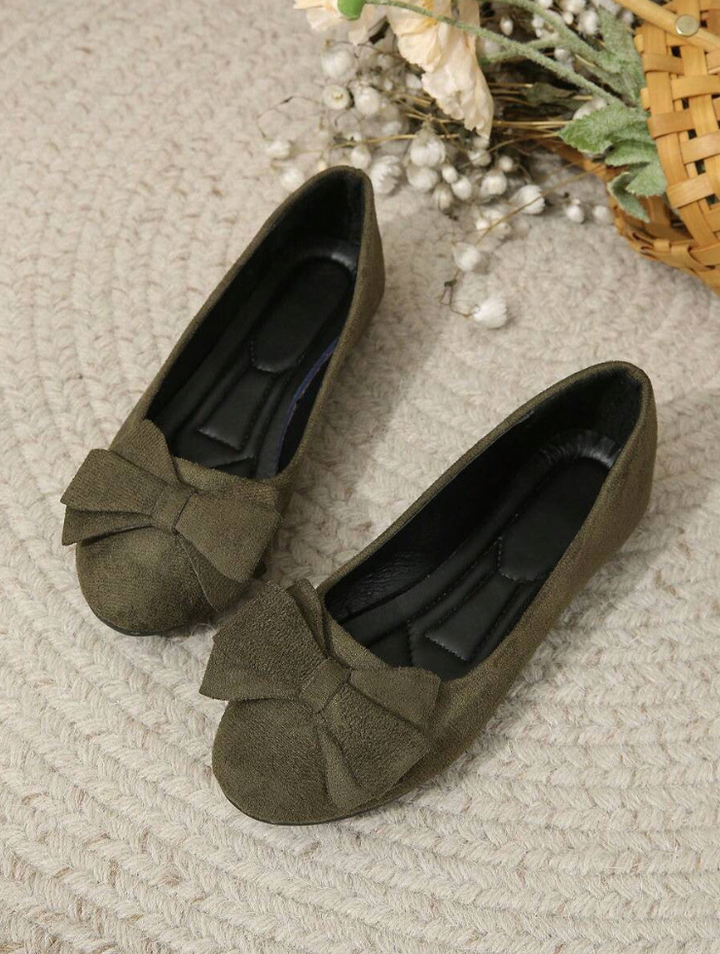 Olive green bow-front ballerina flats displayed on woven rug