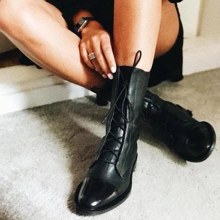 Black leather ankle boots with lace-up fastening, being adjusted by hand while seated