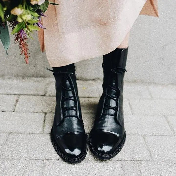 Black leather ankle boots with patent toe cap, worn beneath a pink midi dress
