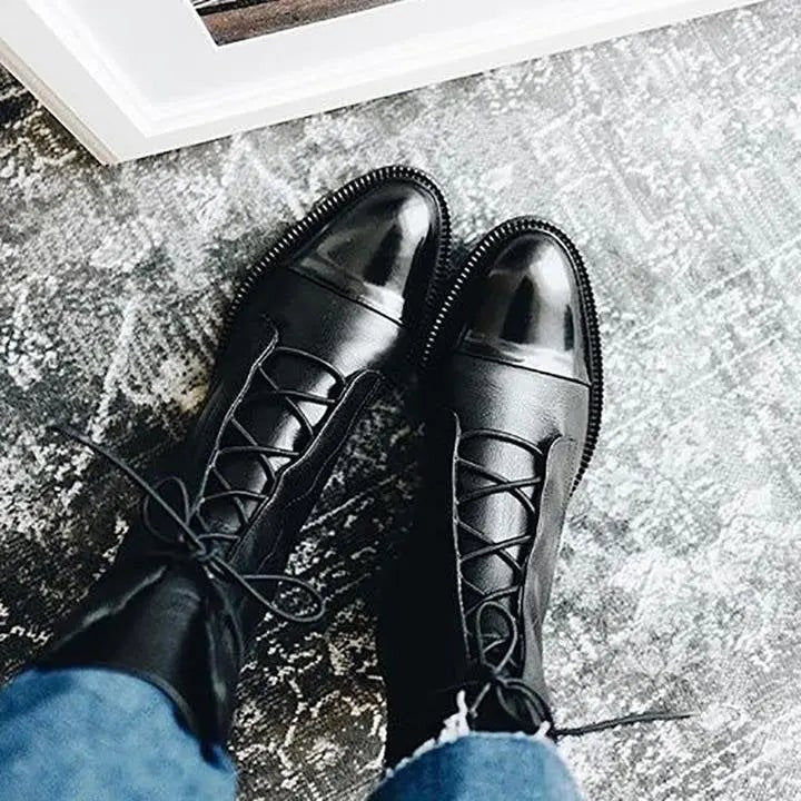 Black leather ankle boots with polished cap toe, viewed from above on patterned rug