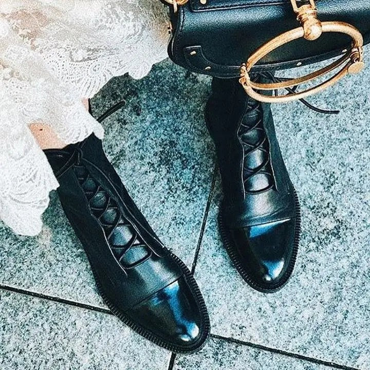 Black leather lace-up ankle boots with shiny toe cap, paired with a structured handbag