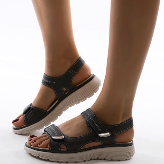Black orthopedic sandals with contrast stitching worn on crossed feet