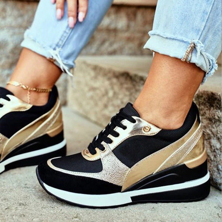 Close-up of black platform sneakers featuring gold metallic side stripes