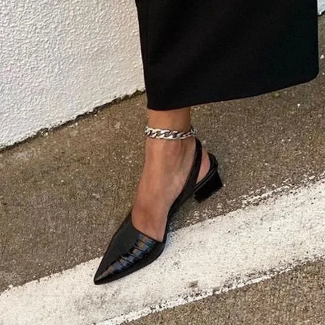 Woman wearing black patent slingback heels with ankle chain accessory