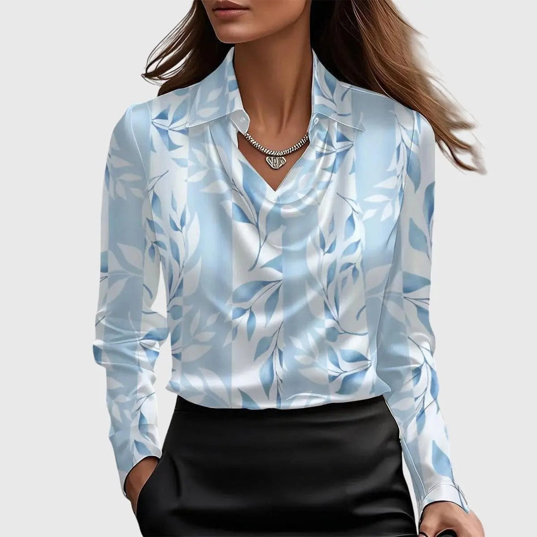 Blue and white leaf-print satin blouse with draped collar, worn over a black skirt