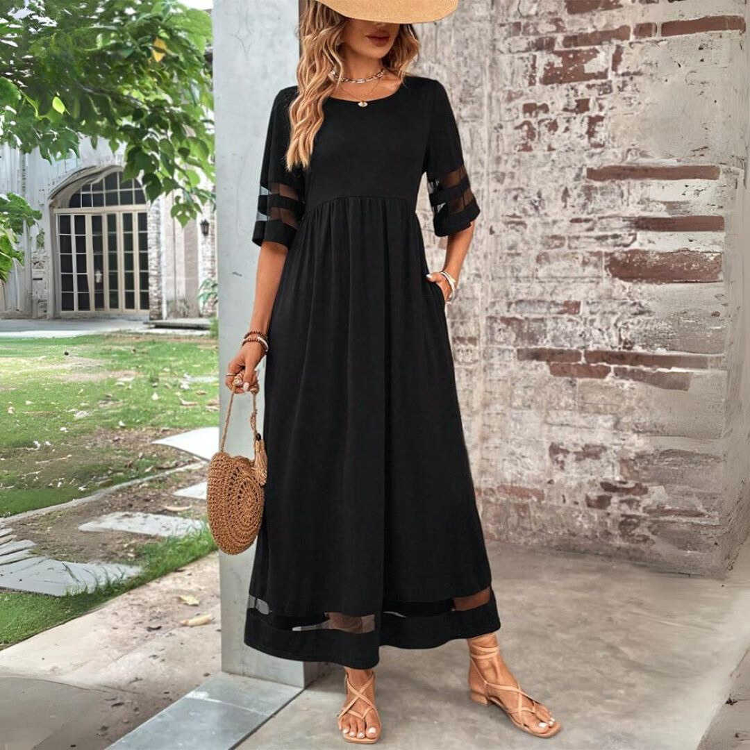 Black maxi dress with sheer mesh panel sleeves and flowing skirt, styled with a straw hat