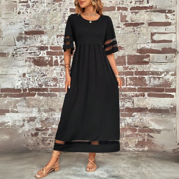 Black maxi dress with mesh panelled sleeves and cinched waist, displayed against brick backdrop