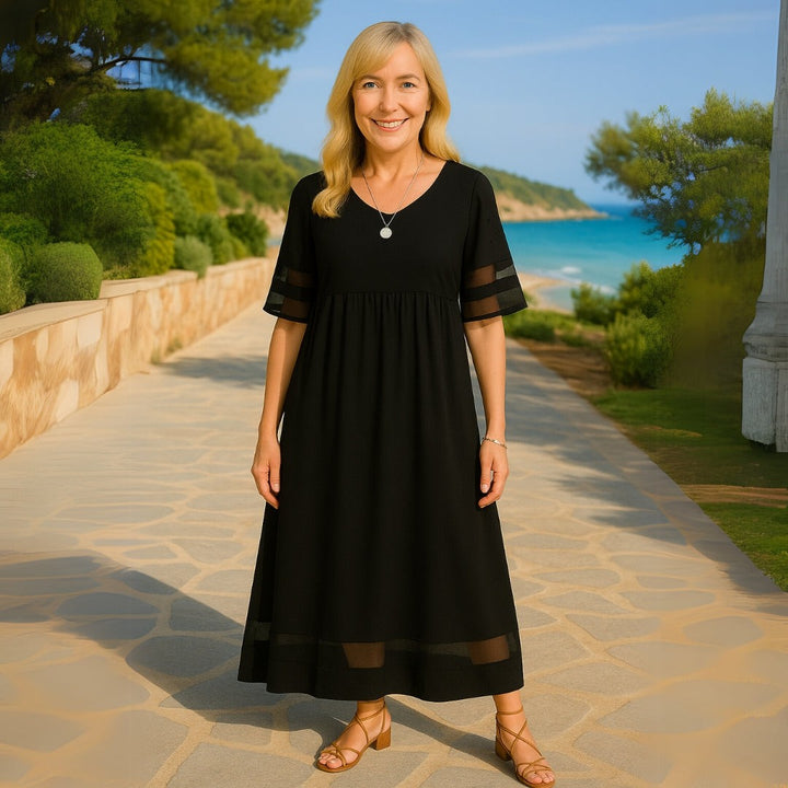 Black midi dress featuring mesh-panelled sleeves and V-neckline, worn on a coastal path