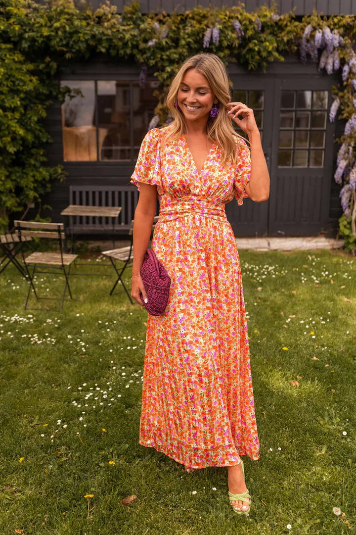 Orange floral maxi dress with flutter sleeves and wrap V-neckline in garden setting