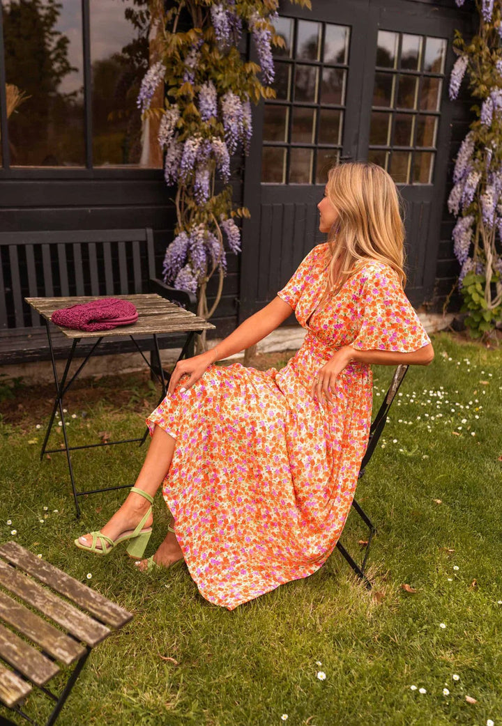 Side view of orange floral maxi dress with cinched waist, seated on garden chair