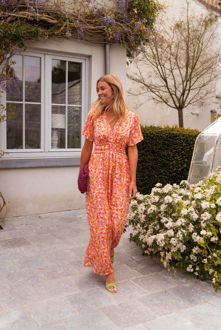 Orange floral maxi dress with flutter sleeves worn against a rustic stone courtyard