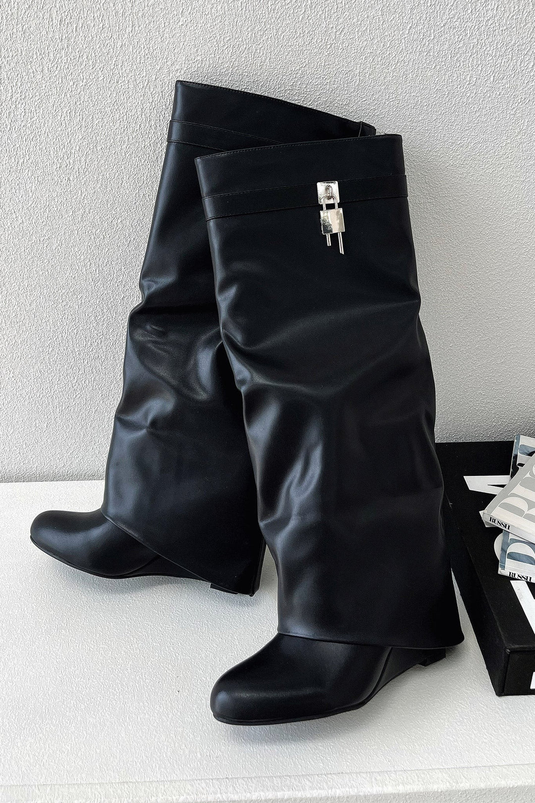 Pair of black knee-high boots showing pointed toe and buckle strap trim