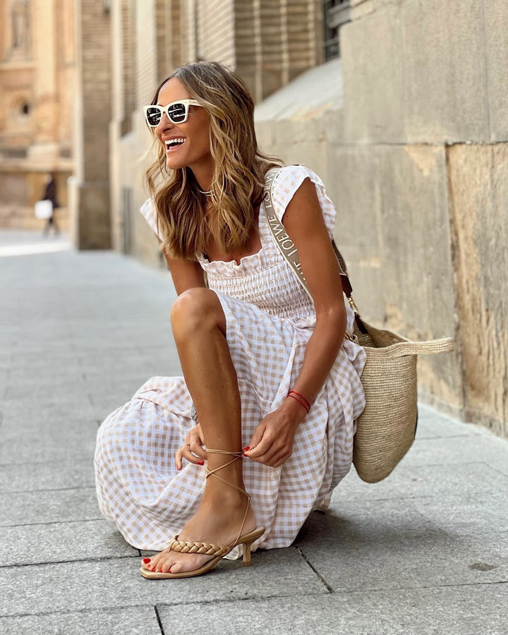 Model tying strappy sandals in beige gingham flutter sleeve maxi dress