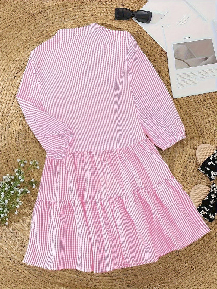 Pink gingham tiered shirt dress laid flat beside sunglasses and slides