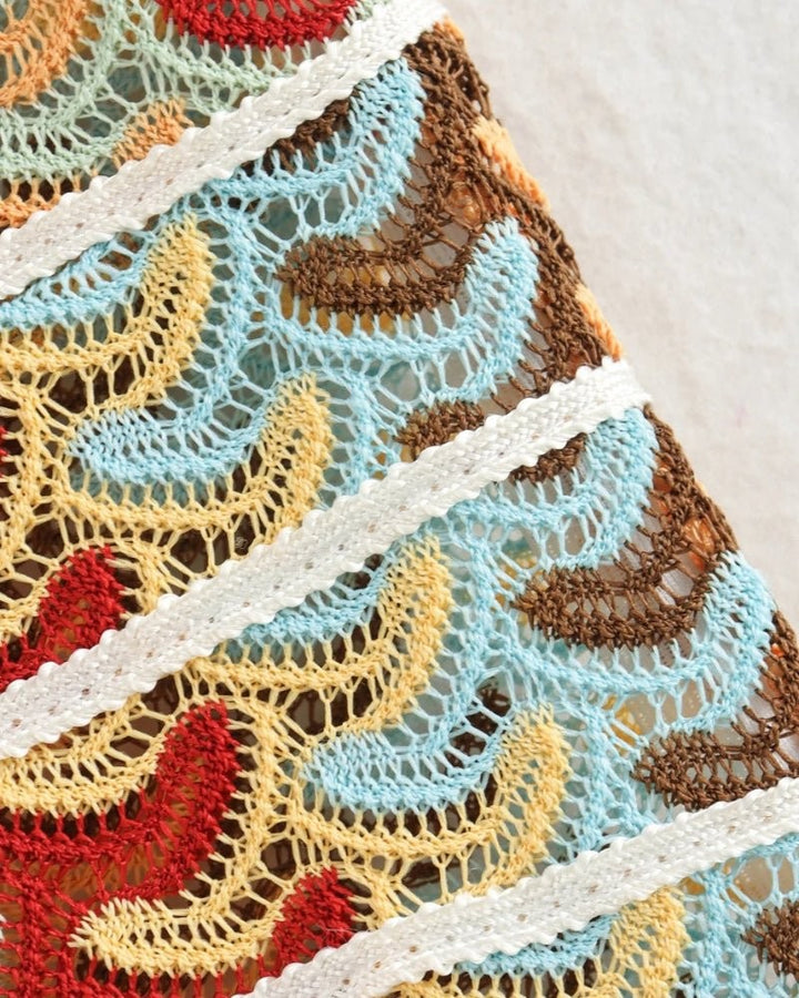 Zoomed detail of crochet-knit fabric with cream ribbon trim and wave pattern
