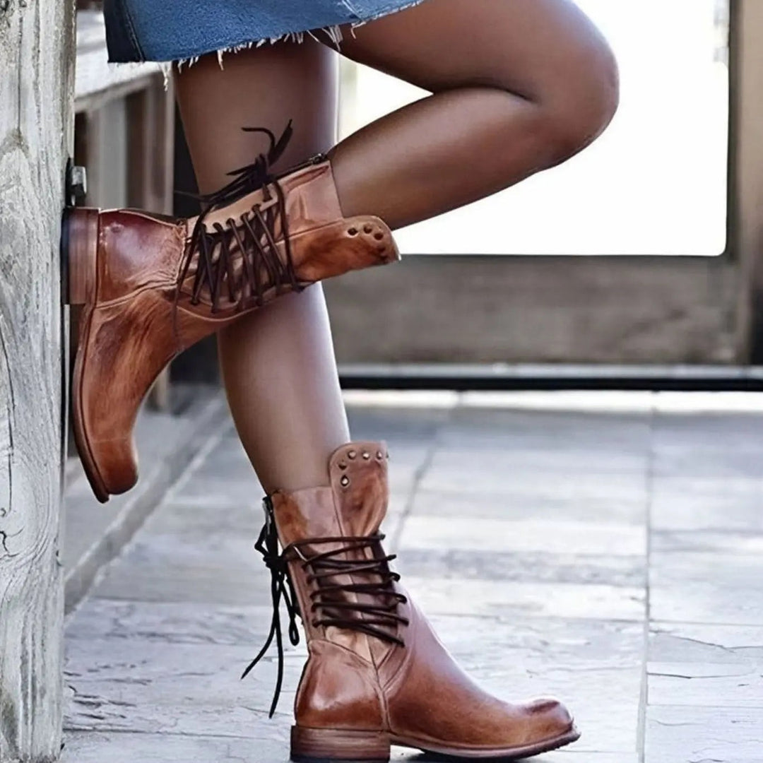 Tan leather lace-up mid-calf boots with studded ankle trim, worn outdoors