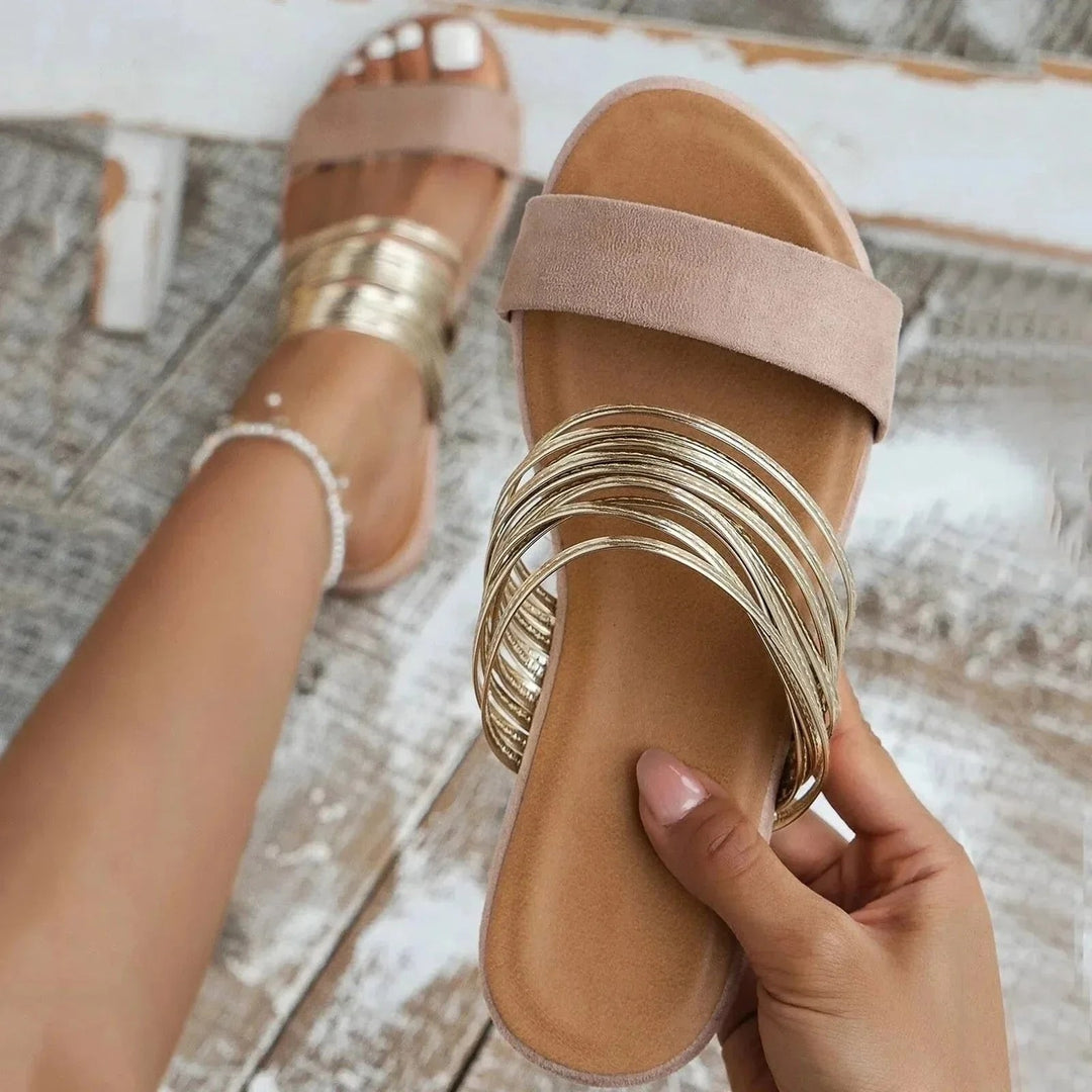 Blush pink flat sandals with multiple slim gold straps across the front