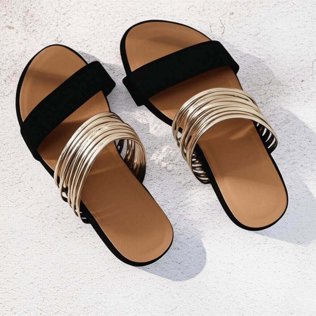 Pair of black suede slide sandals with gold multi-strap design against pale backdrop