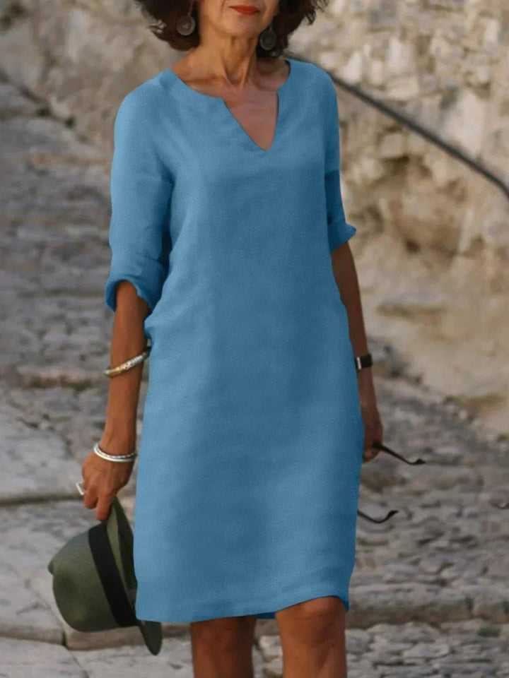 Sky blue V-neck midi dress with mid-length sleeves, worn on stone steps