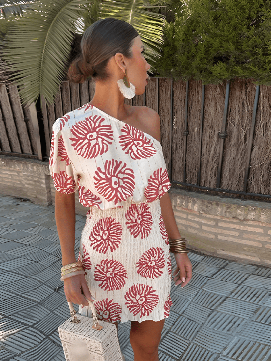 One-shoulder mini dress in cream with red floral print, worn poolside