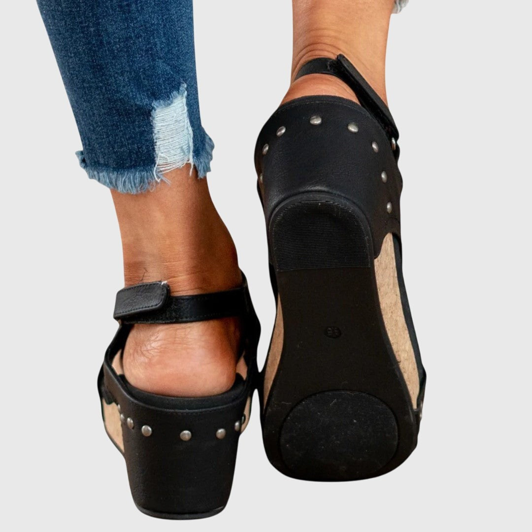 Rear view of black studded wedge sandals displaying cork sole and buckle strap