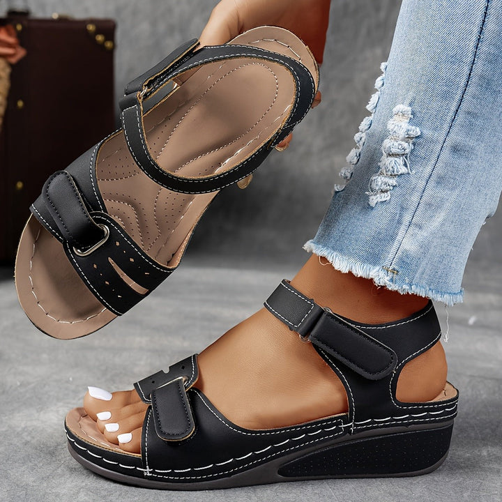 Black open-toe wedge sandal featuring cushioned footbed and hook-and-loop straps