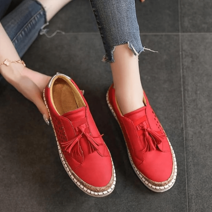 Red slip-on loafers with tassel trim viewed from above on model's feet