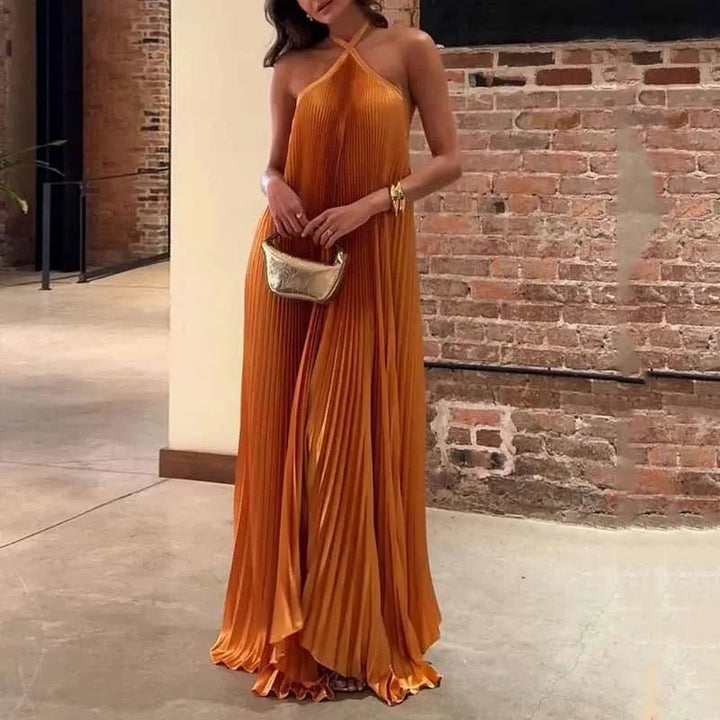 Burnt orange pleated halter maxi dress with flowing satin skirt, worn against brick wall