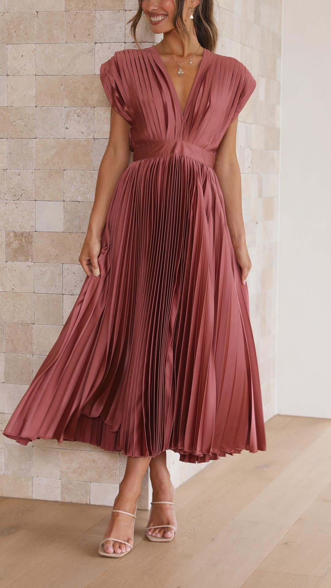 Model twirling in rust pleated satin dress showing flowing pleated skirt