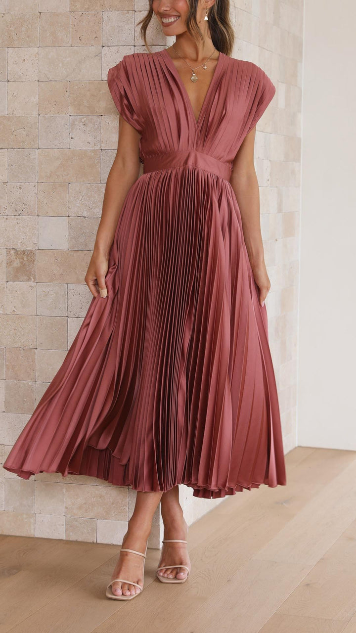 Model twirling in rust pleated satin dress showing flowing pleated skirt