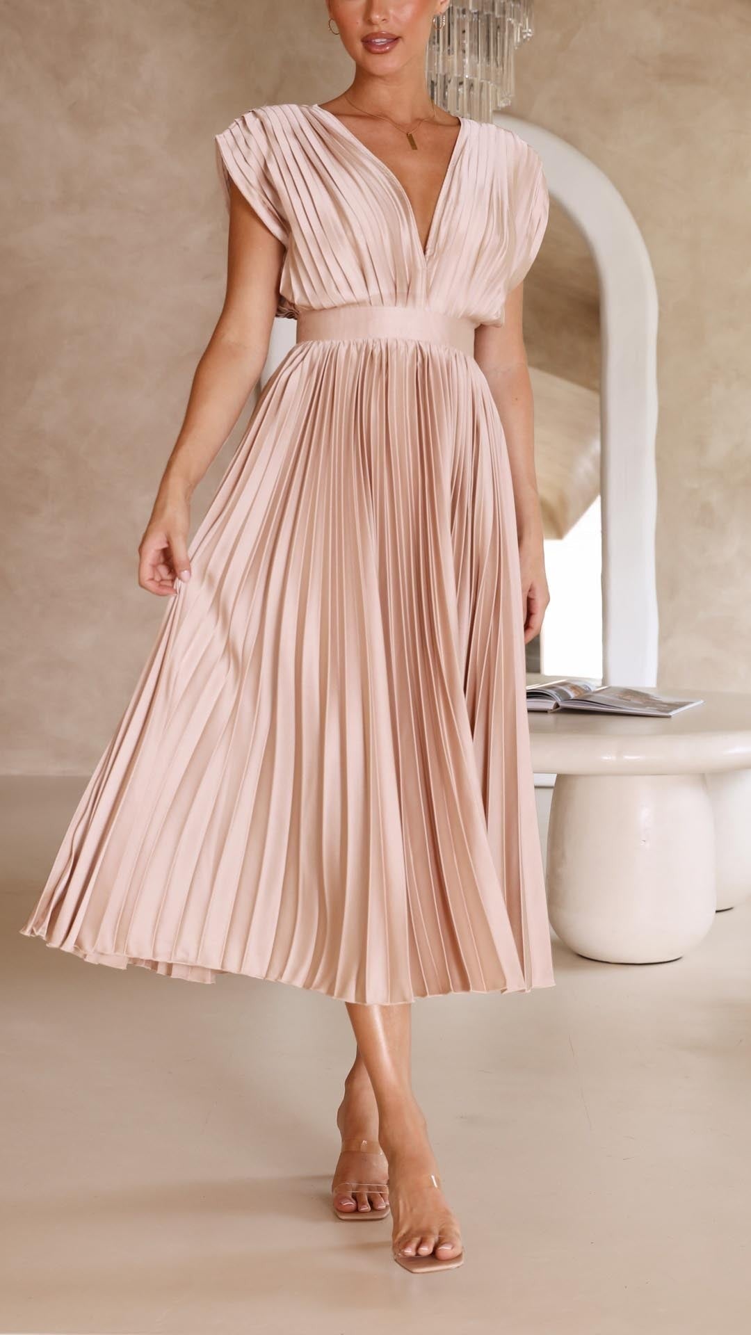 Side view of blush pleated satin dress paired with clear strap heels