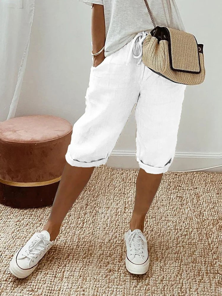 White linen turn-up trousers styled casually with white trainers and a woven bag