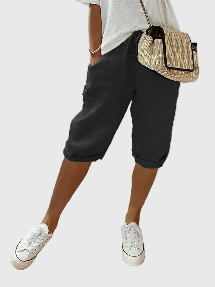 Black turned-up cropped trousers with drawstring waist, worn with white trainers