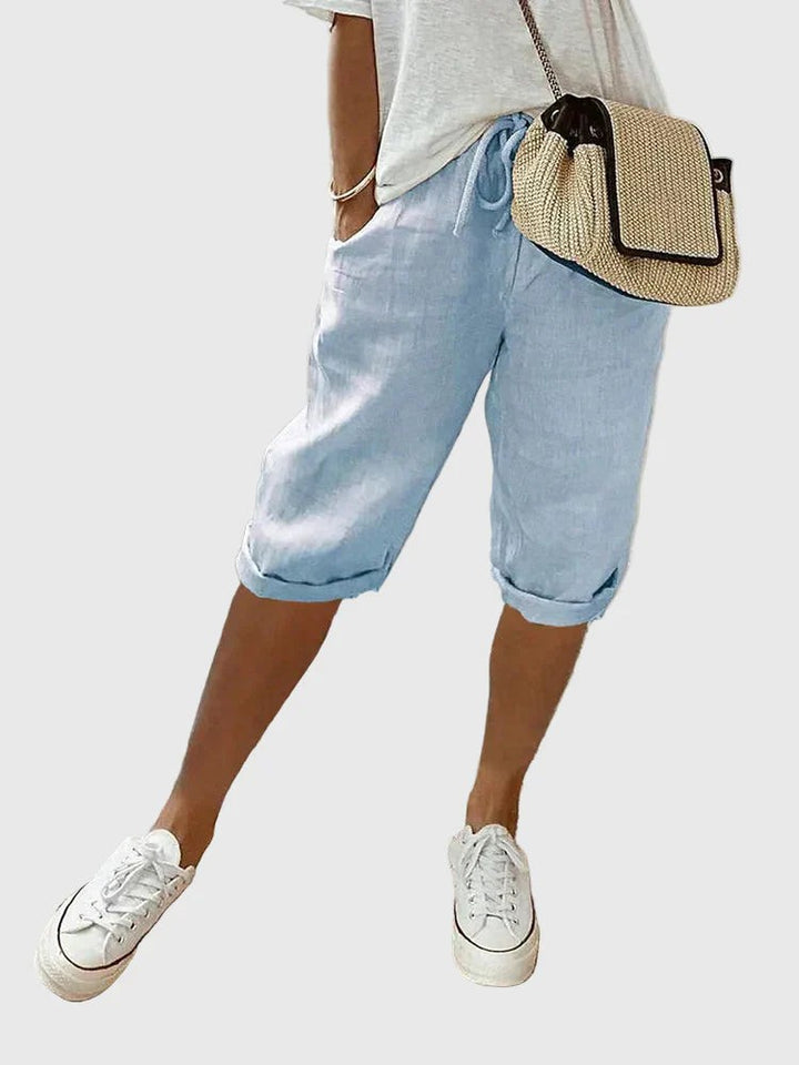 Pale blue linen cropped trousers styled with rolled hems and white trainers