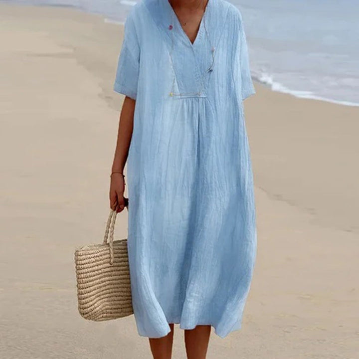 Pale blue linen-style midi dress with V-neck, worn on a beach
