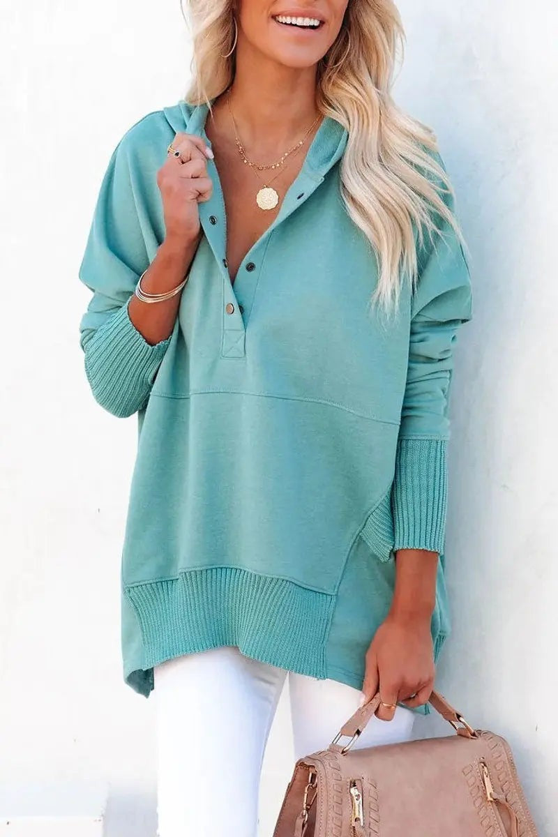 Teal hooded pullover with snap placket paired with white trousers