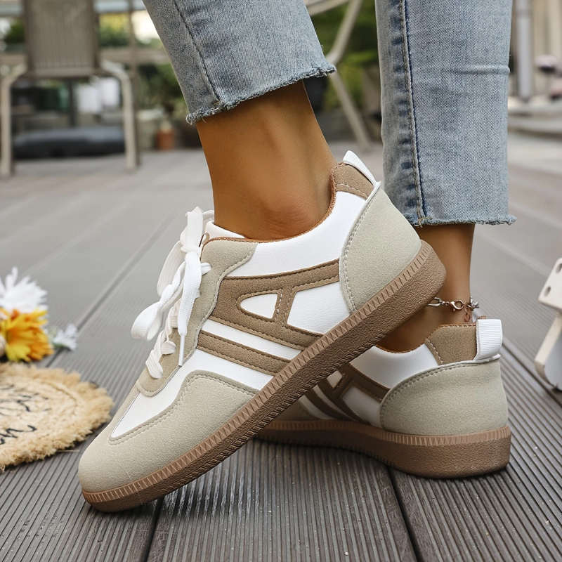 White and beige lace-up sneakers featuring tan stripe detailing on a wooden deck