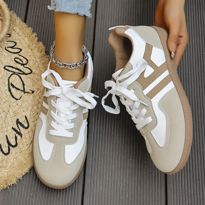 Beige and white lace-up sneakers with tan accents held in hand outdoors