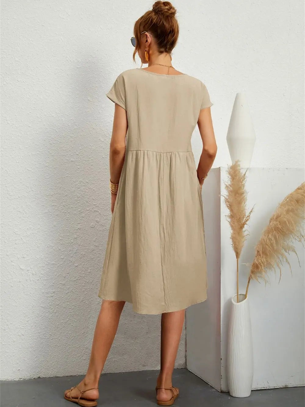 Rear view of beige midi dress highlighting flowy pleated skirt and loose sleeves