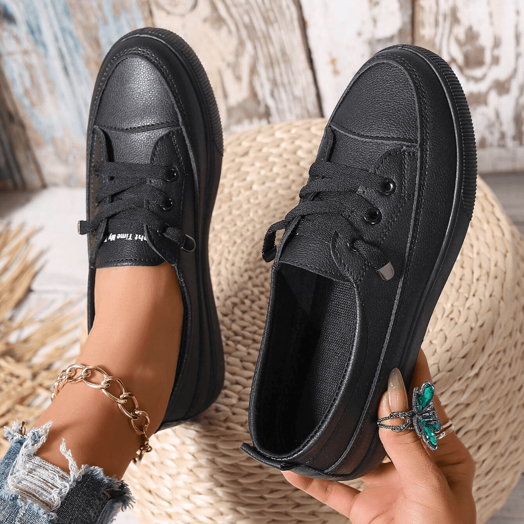 Pair of black lace-up flatform trainers held by hand, showing stitched detailing