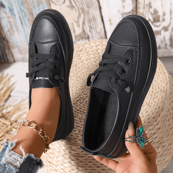 Pair of black lace-up flatform trainers held by hand, showing stitched detailing