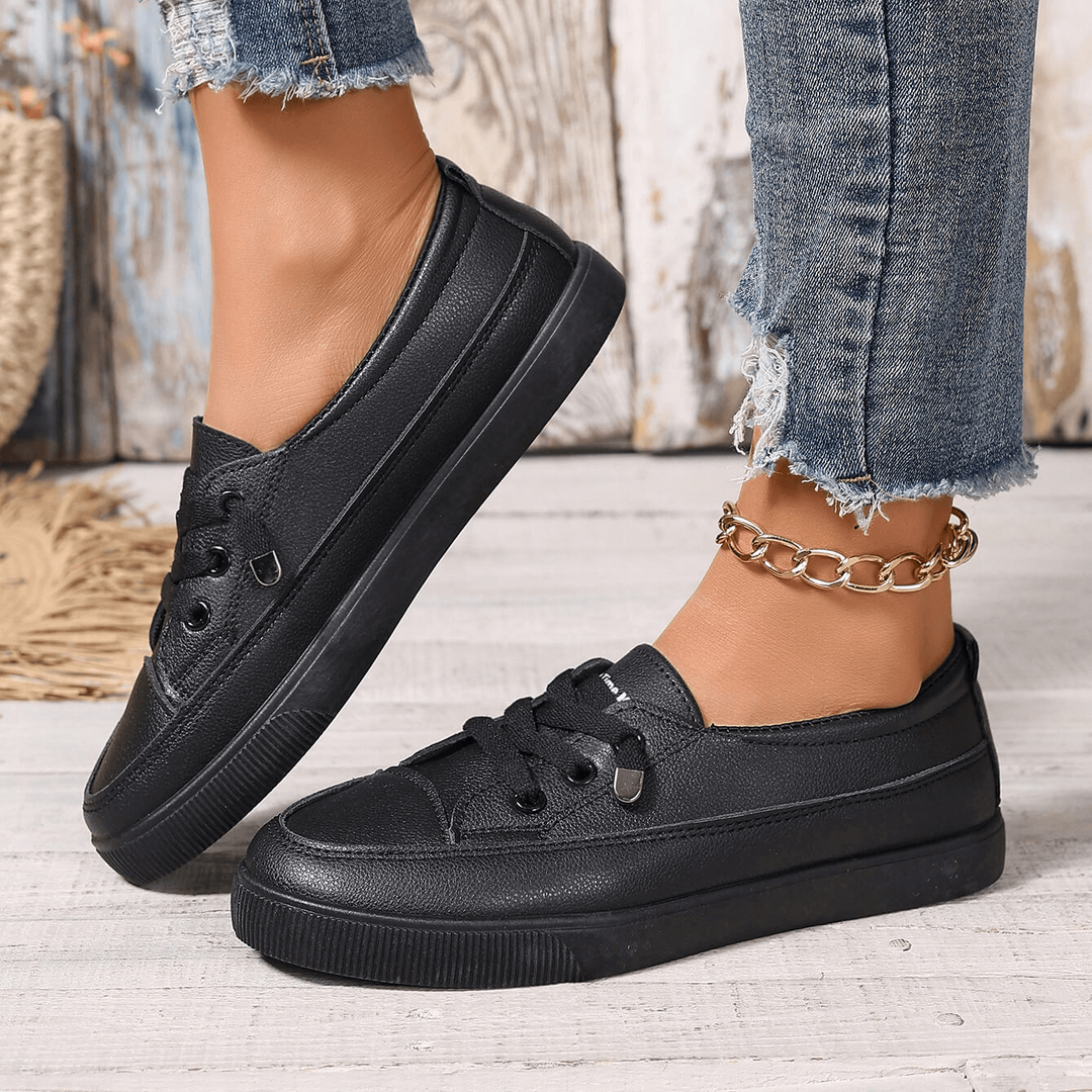 Black flatform lace-up trainers shown from behind with gold chain anklet