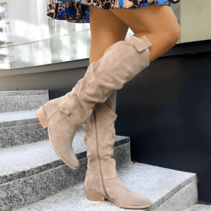 Beige suede slouch knee boots with buckle strap, worn on stairs