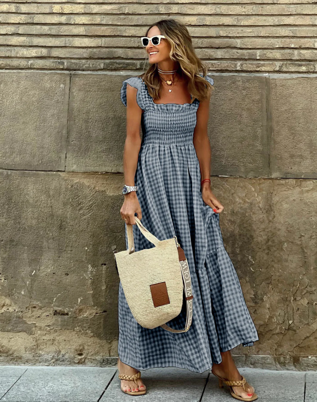 Blue check smocked maxi dress worn against stone wall with woven tote