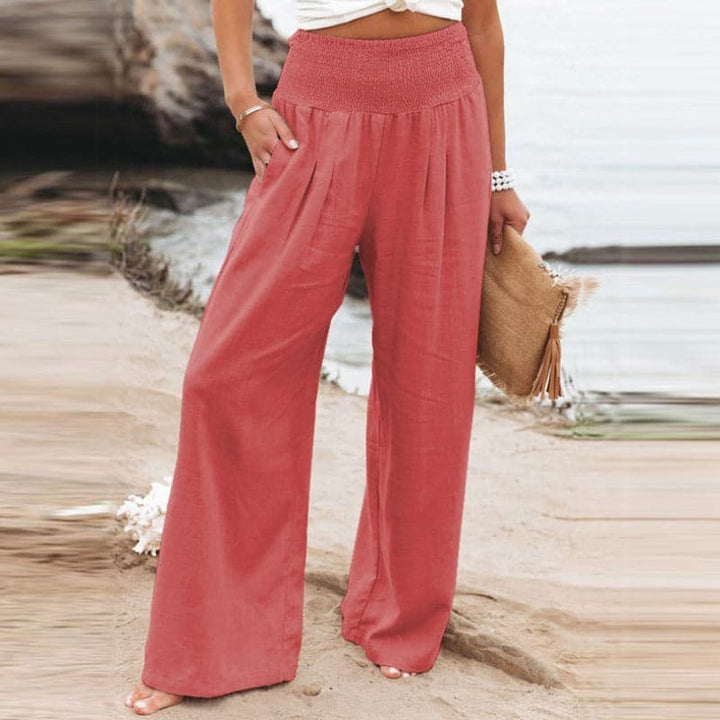Coral pink wide-leg trousers with smocked high waist, worn on sandy beach