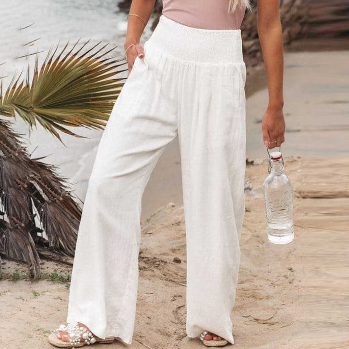 White wide-leg linen trousers with smocked high waist, coastal backdrop