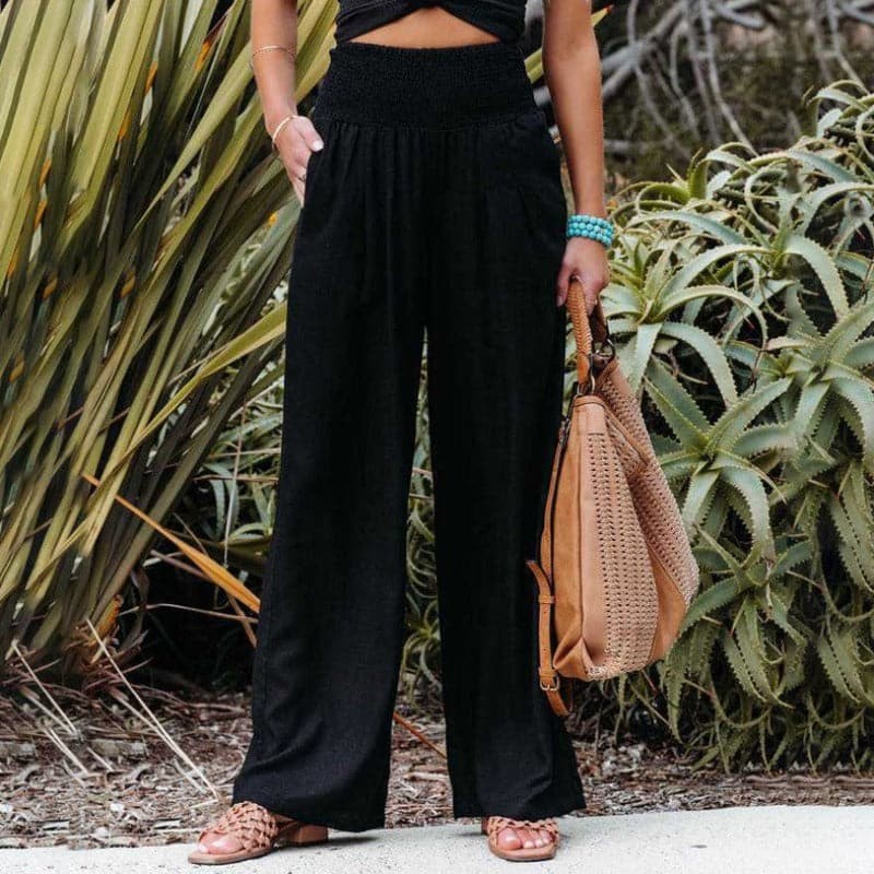 Black wide-leg trousers with smocked high waist, styled with tan handbag