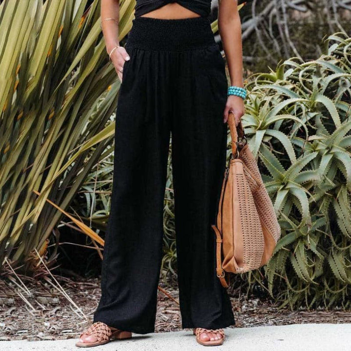 Black wide-leg trousers with smocked high waist, styled with tan handbag