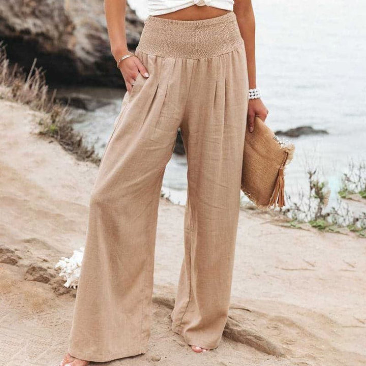 Beige wide-leg linen trousers with smocked waist, paired with straw clutch