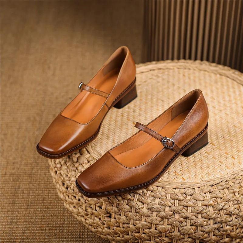 Pair of tan leather Mary Jane shoes with block heels displayed on straw stool